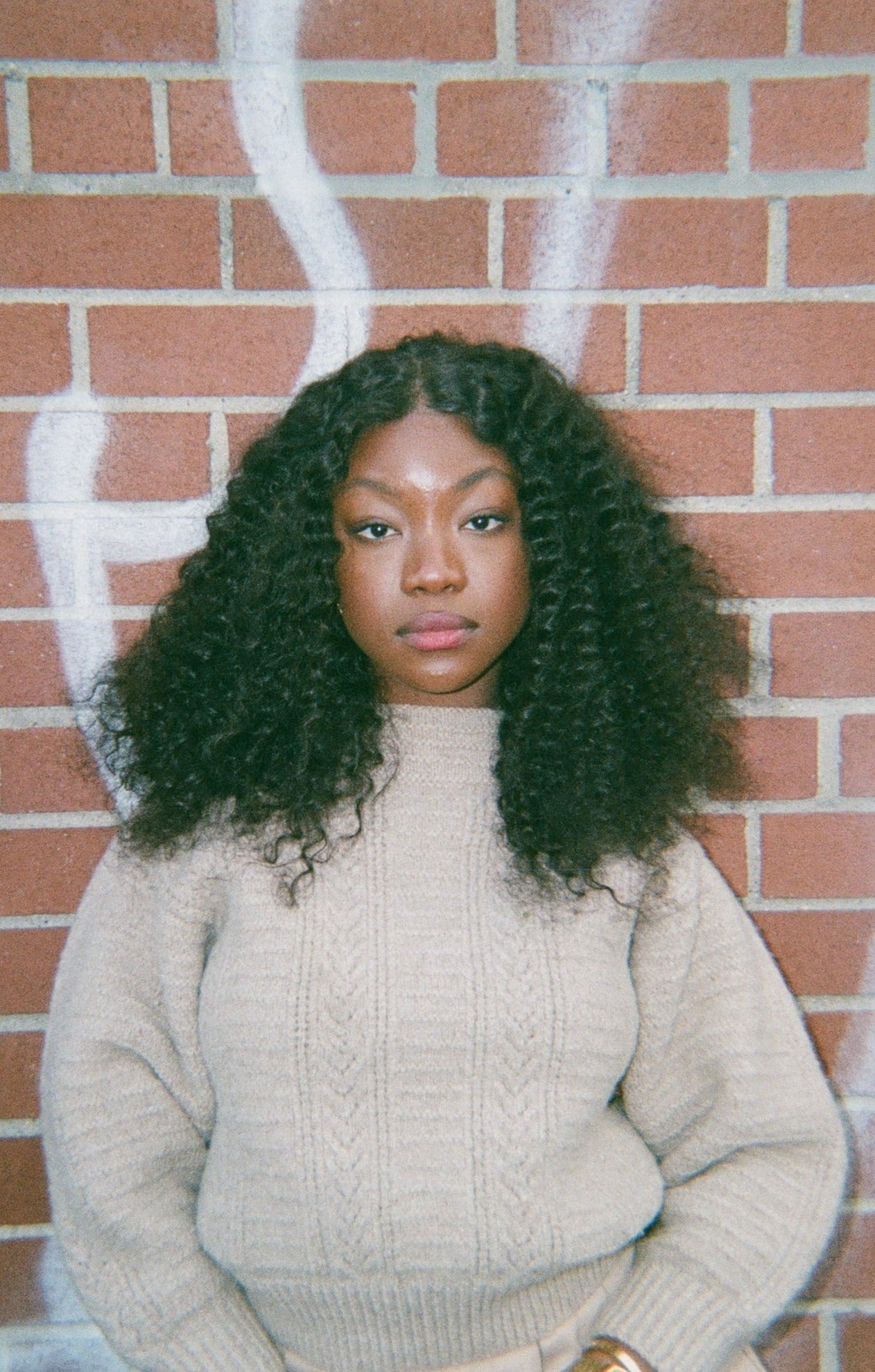 A woman posing in front of a brick wall, showcasing her stylish curly black human hair wig.