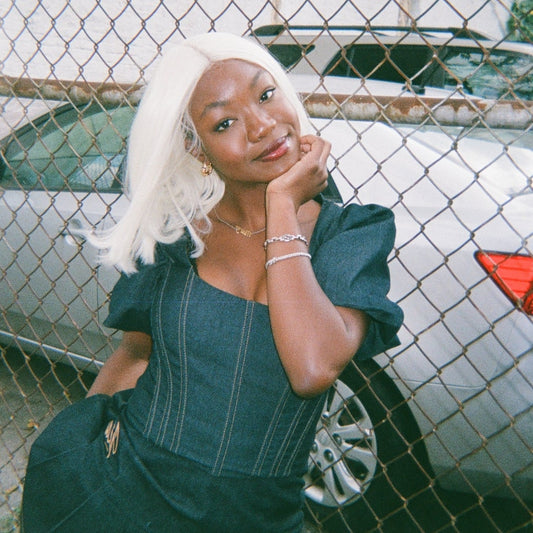 Woman with platinum blonde synthetic hair wig posing in front of a fence.