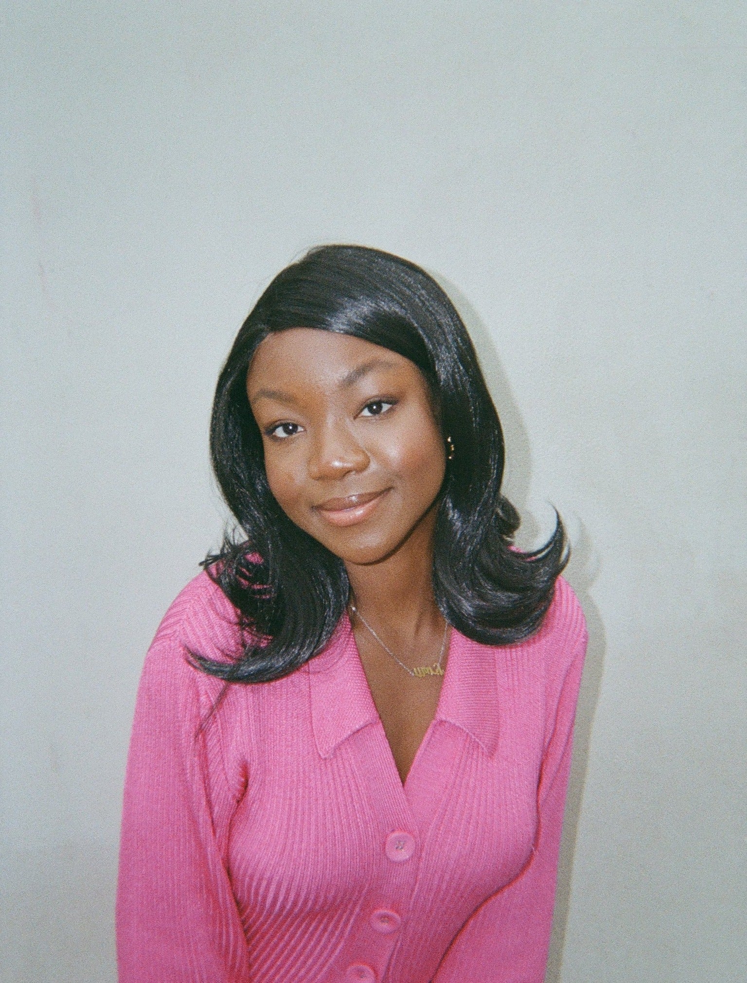 A stylish woman wearing a pink outfit poses for a photo, her black synthetic hair wig with flipped ends completing her trendy outfit.