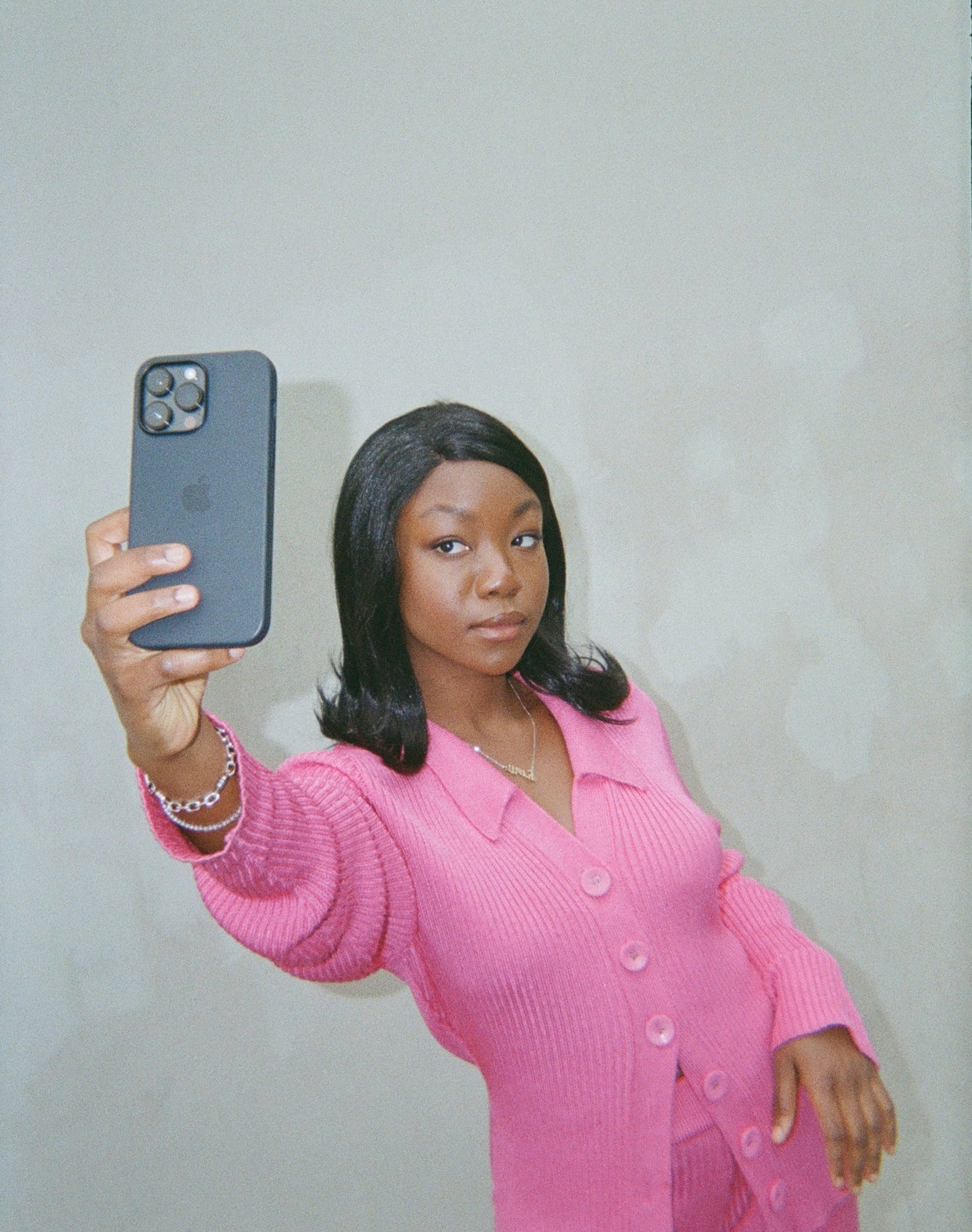 A stylish woman wearing a pink outfit poses for a selfie, her black synthetic hair wig with flipped ends completing her trendy outfit.