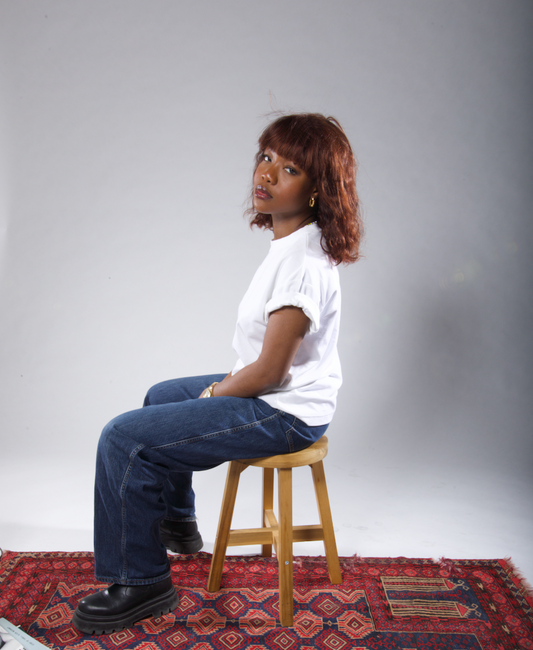 A woman sitting on a stool, wearing a stylish brown human hair wig with bangs.